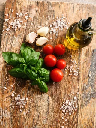 Basilico, aglio, pomodorini e olio d'oliva su un tagliere di legno