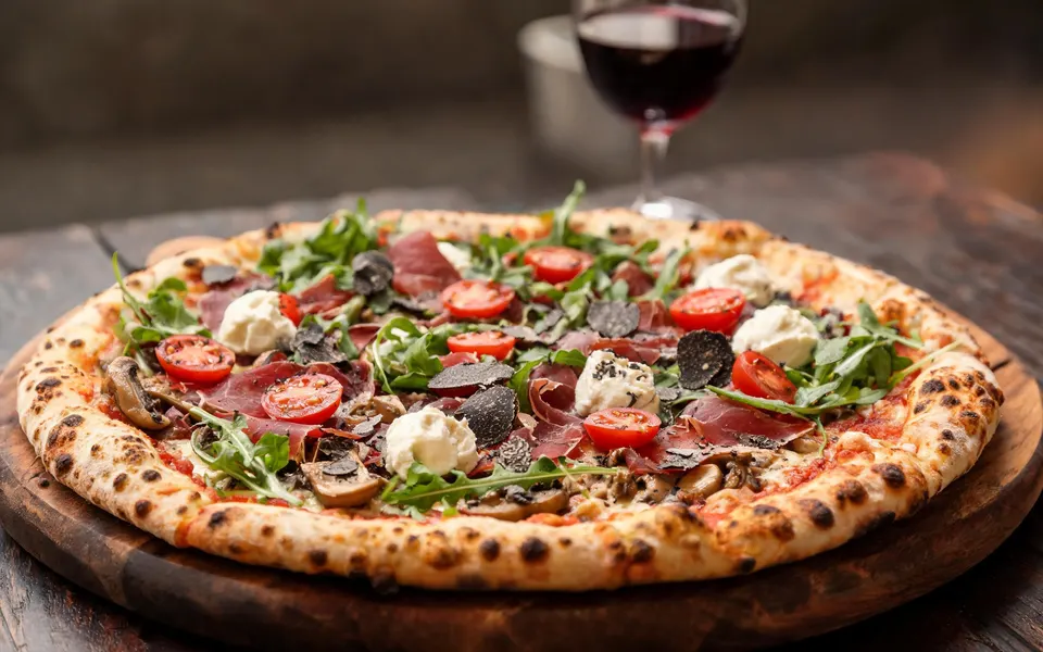 Pizza con bresaola, rucola, pomodorini, mascarpone e scaglie di tartufo su un tagliere di legno