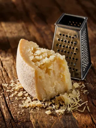Un pezzo di parmigiano con grattugia e scaglie fresche su legno